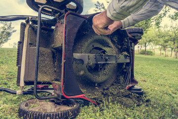 Man cleaning lawn mower blade. - obrazy, fototapety, plakaty