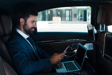 Great email. Side view of handsome young man using laptop and using his smart phone while sitting in car