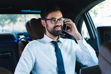 Perfect agreement. Handsome young man talking on mobile phone with smile while sitting in car