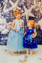 
Two little girls sitting near the Christmas tree and wait for the New year