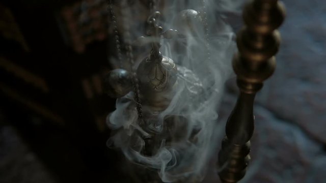 Smoke from incense and cross in Catholic church indoors. Gray fragrant fume rises up and gently wraps space above metal cross that is seen in center of the ritual composition. Tranquil atmosphere in