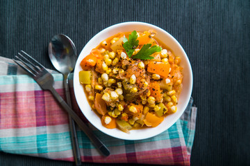 Vegetable stew with corn, sweet pepper, zucchini in a white plate on the table, top view
