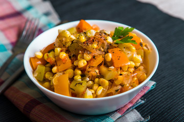 Vegetable stew with corn, sweet pepper, zucchini in a white plate on the table, top view
