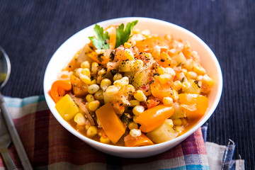 Vegetable stew with corn, sweet pepper, zucchini in a white plate on the table, top view
