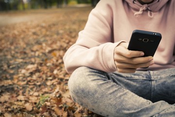 young teenager with mobile phone in the park in the fall