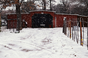 Rural farm winter with snow on drive to red barn, trees and nature in background of building.  Snow...