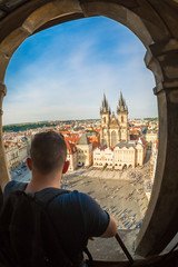 Tourism in Europe. Young man is looking to the buildings on the Old Town square Staromestska Namesti from old astronomical clock tower Orloj in Prague, Czech Republic. Fish-eye lens