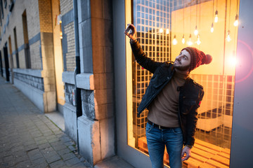 Fototapeta na wymiar Happy hipster guy making selfie photo against the background of lamps.