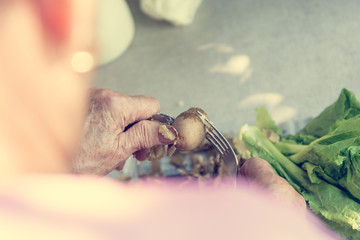 Closeup of elderly hands peaing potatoe.