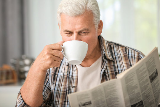 Handsome mature man reading newspaper in kitchen