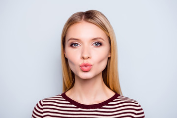 Obraz premium Close up portrait of amazing woman pulled her lips to kiss someone, blowing kiss to camera, sending kiss with full lips, gives a kiss, standing over grey background