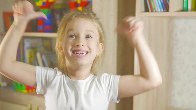 Funny little girl in singing standing in children's room, moving and laughing