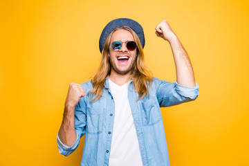 Happy lottery winner. Portrait of handsome guy raising fists up in casual wear celebrating victory standing over yellow background
