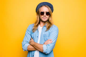 Closeup portrait of handsome confident young student is standing on the yellow background, he is serious, crossed his arms. Guy is wearing casual outfit, people concept