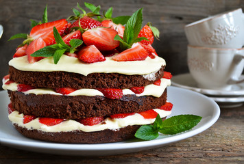 Naked cake with cream, decorated with strawberry, mint and chocolate on a black background