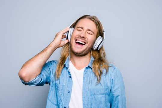 Close up portrait of caucasion bristle guy listening his favorite music, singing the song, holding  earphones on the head standing over grey background