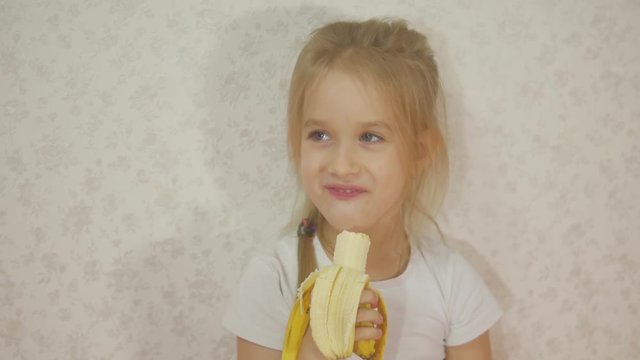 Young girl eating banana sitting at home.