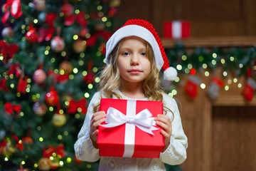 Little girl sitting by the tree holding a Christmas gift In the 