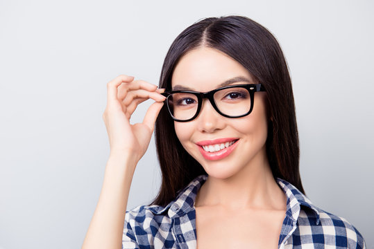 Close up portrait of charming smart lady with toothy smile, hazel eyes and beautiful face is touching her spectacles, dressed in casual checkered clothes isolated on grey background