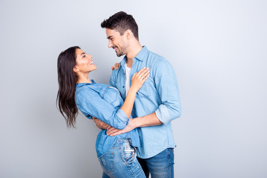 This sweety love makes my head spin! Handsome joyful happy man in casual clothes is hugging her girlfiend's waist, isolated on grey background