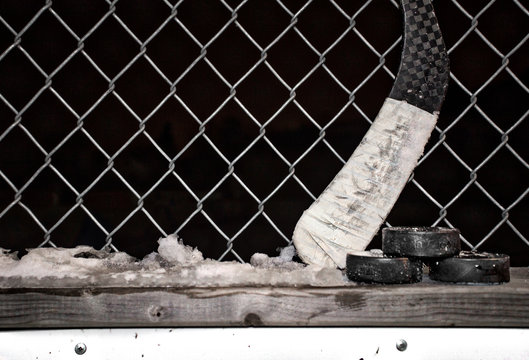 Black Hockey Pucks And Blade Of A Hockey Stick Leaning Against A Wire Fence