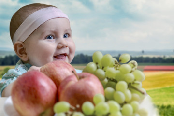 Fototapeta na wymiar positive kid smiles and rejoices in front of the table with fresh fruit on the background of the countryside