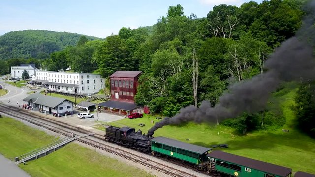 Aerial camera follows a Cass Scenic Railroad train pulls several tourist cars backwards as it moves toward the station for passengers.