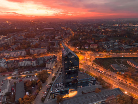 Modern architecture office building, Transportation, rush hour traffic, cars on highway interchange in city center. Sunset time, orange and gold light skyline. Drone aerial view of Krakow, Poland. 