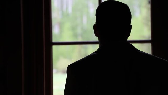 Silhouette man stands by window in contemplation, close up.