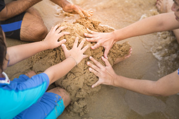 The girl child and parents are using their hands to pile sand on the beach, which is a time to...