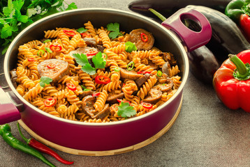 Mediterranean eggplant pasta in pot with tomatoes, red pepper and parsley on grey background.