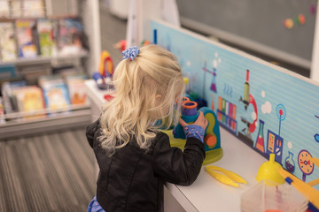 Fototapeta na wymiar Young girl playing with toy microscope in science play center