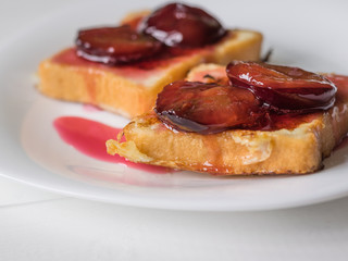 Two pieces of French toast drizzled with plum jam on a white plate.