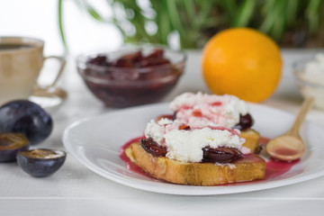 Toasted French bread with plum jam and a wooden spoon on a white plate.