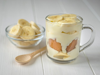 Banana pudding in a glass mug and a small spoon of light wood on the table.