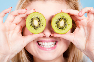 Woman holding green kiwi fruit like eyeglasses