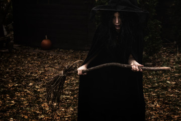 Wicked looking witch holding a broom in a rural autumn scene.