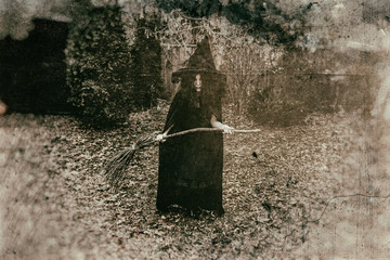 Insidious witch holding a broom in a rural setting, heavily edited with vintage film effects.