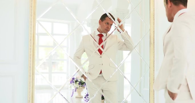 groom looks in the mirror / businessman looks at his reflection in the mirror