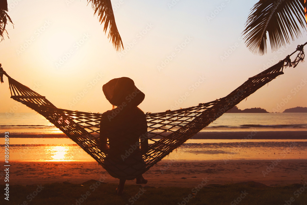 Wall mural beach holidays, silhouette of woman in hat at sunset in hammock, happy vacation