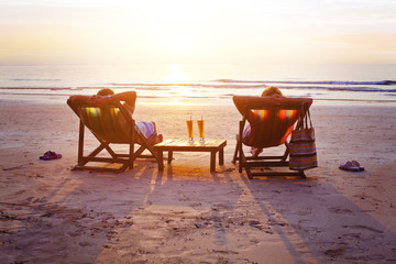 honeymoon travel, silhouettes of happy couple relaxing in deck chairs on the beach at sunset