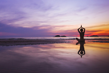 mindful meditation background, silhouette of woman doing yoga on the beach at sunset with reflection