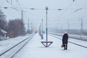 Woman waiting for train in winter blizzard - obrazy, fototapety, plakaty