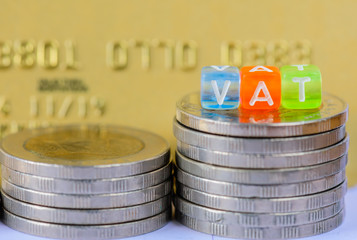 VAT (Value Added Tax) on stacks of  coins with gold credit card background.