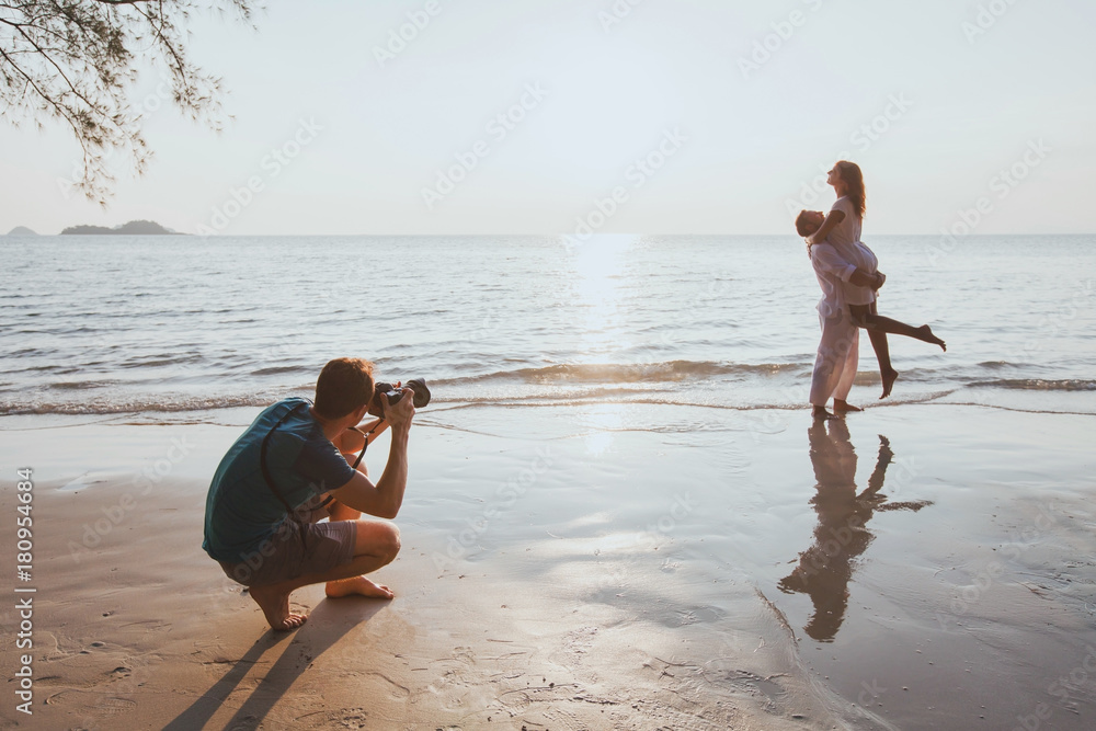 Wall mural wedding and lifestyle photographer taking photos of affectionate couple on the beach at sunset