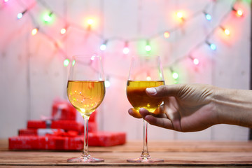 celebration on christmas . adult hand holding a glass of wine , gift boxes on wood table with electric blinker illumination on backdrop