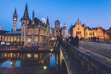 Naklejka na ściany i meble Ghent, Belgium - December 27th, 2016. Saint Michael's bridge panoramic view with merchant houses on Graslei street, Saint Nicholas church and Clock Tower. Gent Old town by Christmas evening lights.