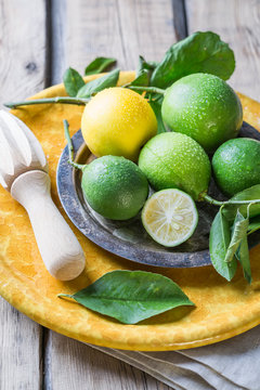 Limes with a lemon on a yellow plate and a wooden table, next to a juicer for citrus.