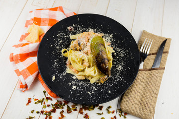 Seafood Pasta with mussels and basil in white plate on wooden table.
