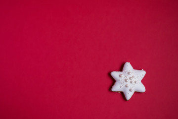 Fototapeta na wymiar Gingerbread star with white icing and sprinkles on red background 